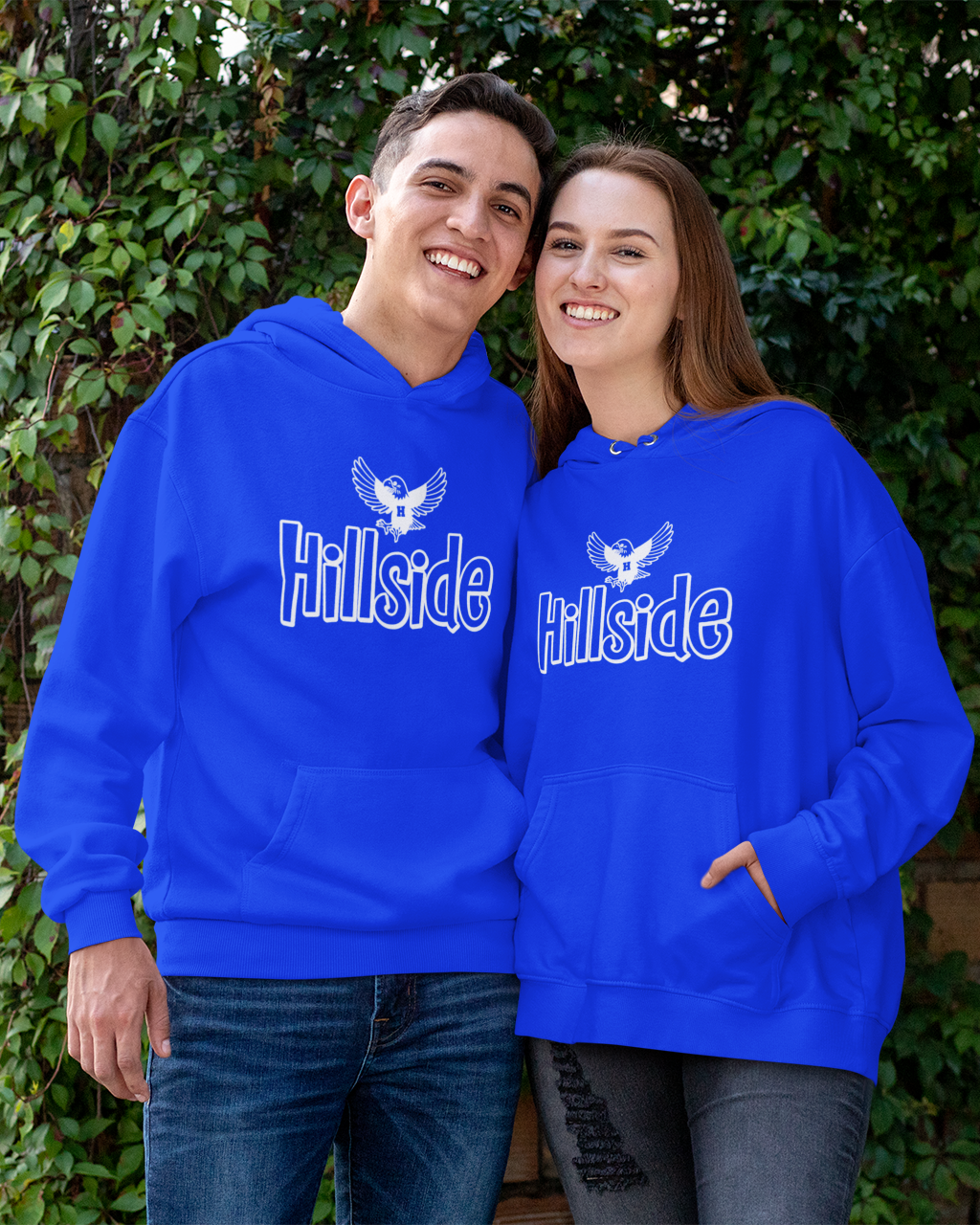 Two people wearing blue 'Hillside' hoodies standing in front of a green leafy background.