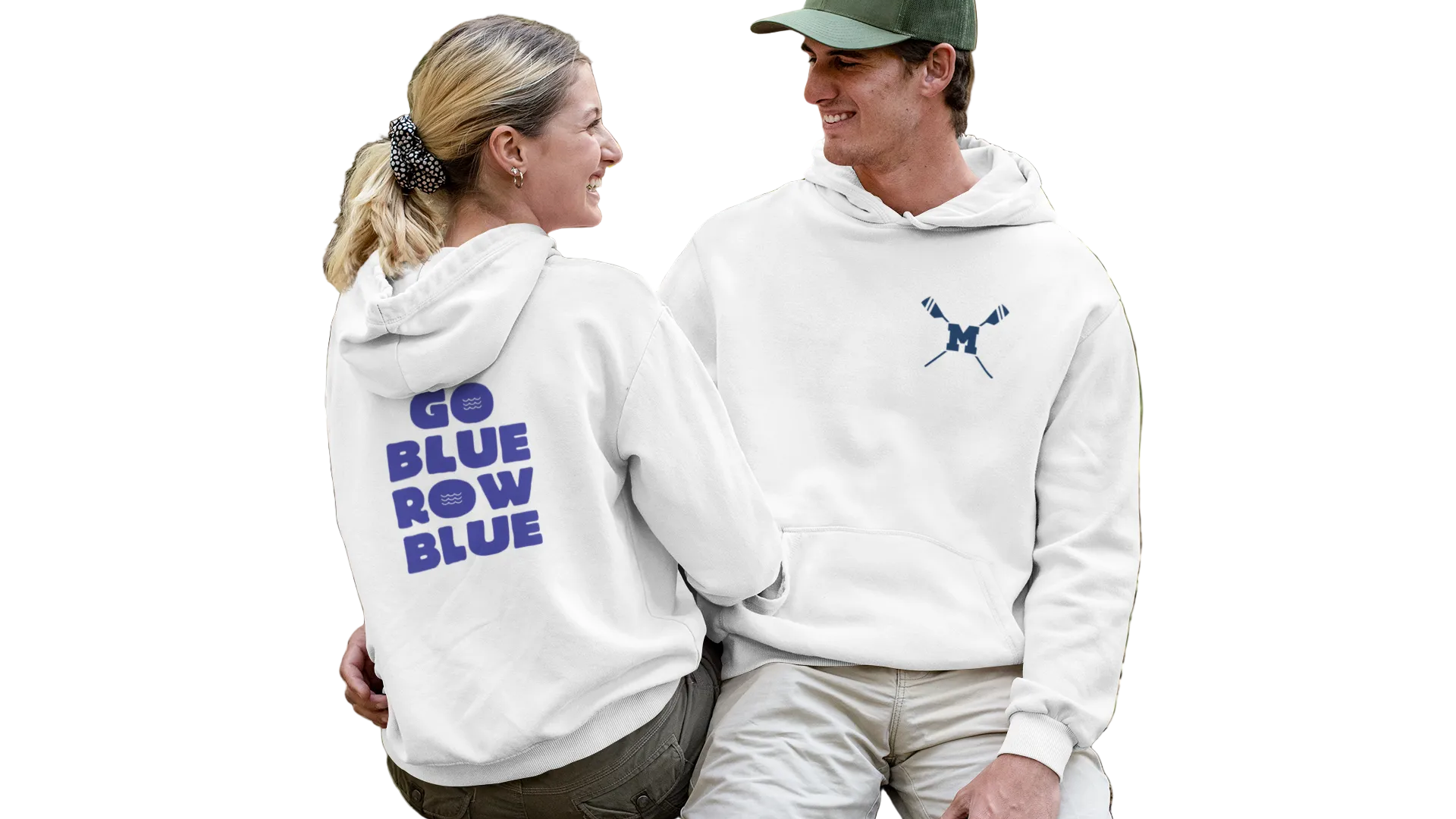 Two people sitting on a log in a forest, wearing matching white hoodies with text and logos.