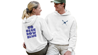 Two people sitting on a log in a forest, wearing matching white hoodies with text and logos.