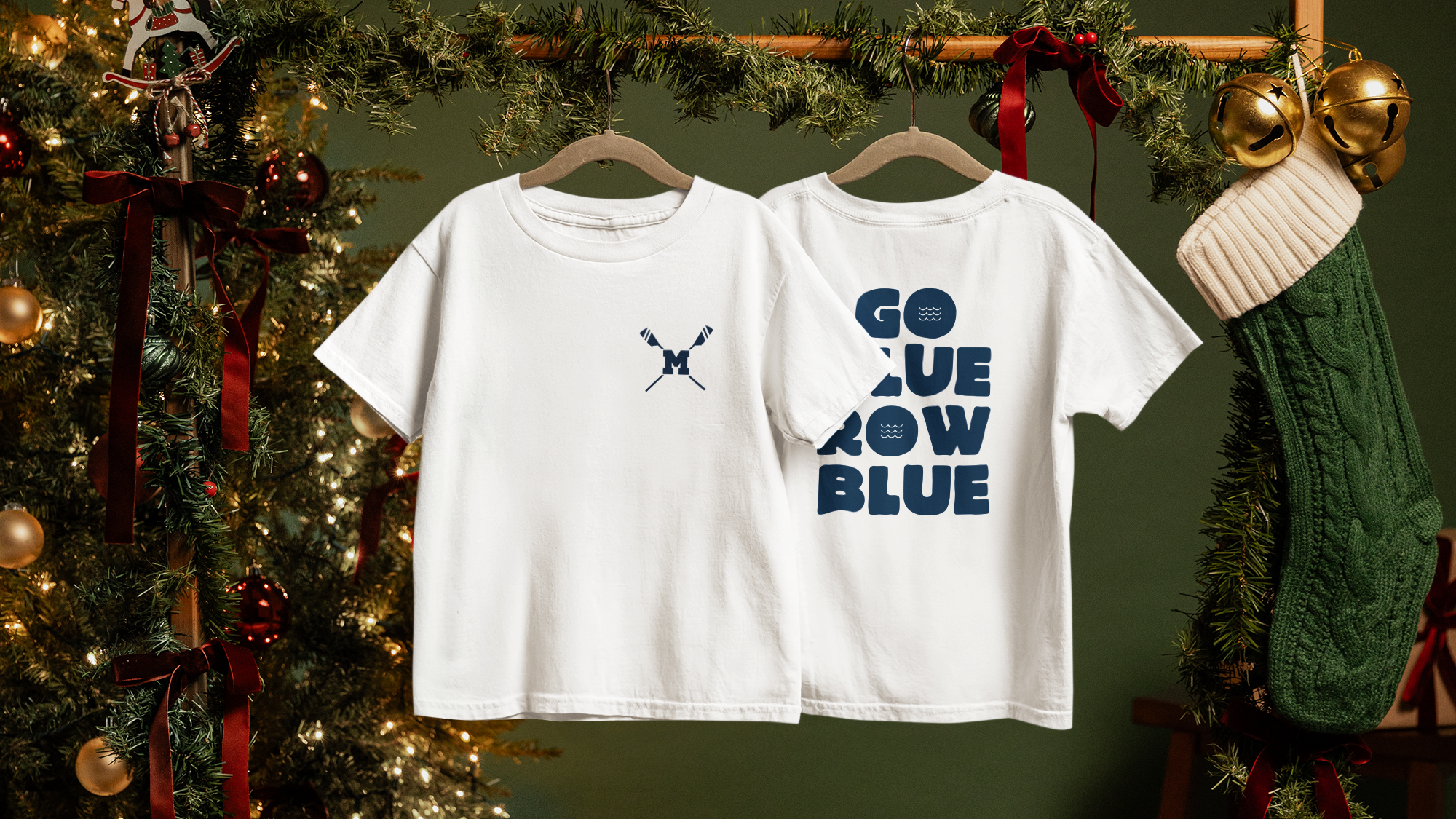 Two white t-shirts with text hanging in front of a decorated Christmas tree.